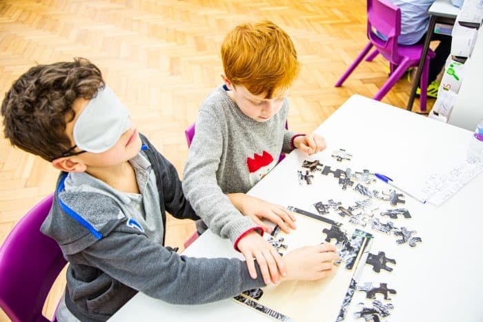 2 kids with puzzle, 1 kid with blindfold
